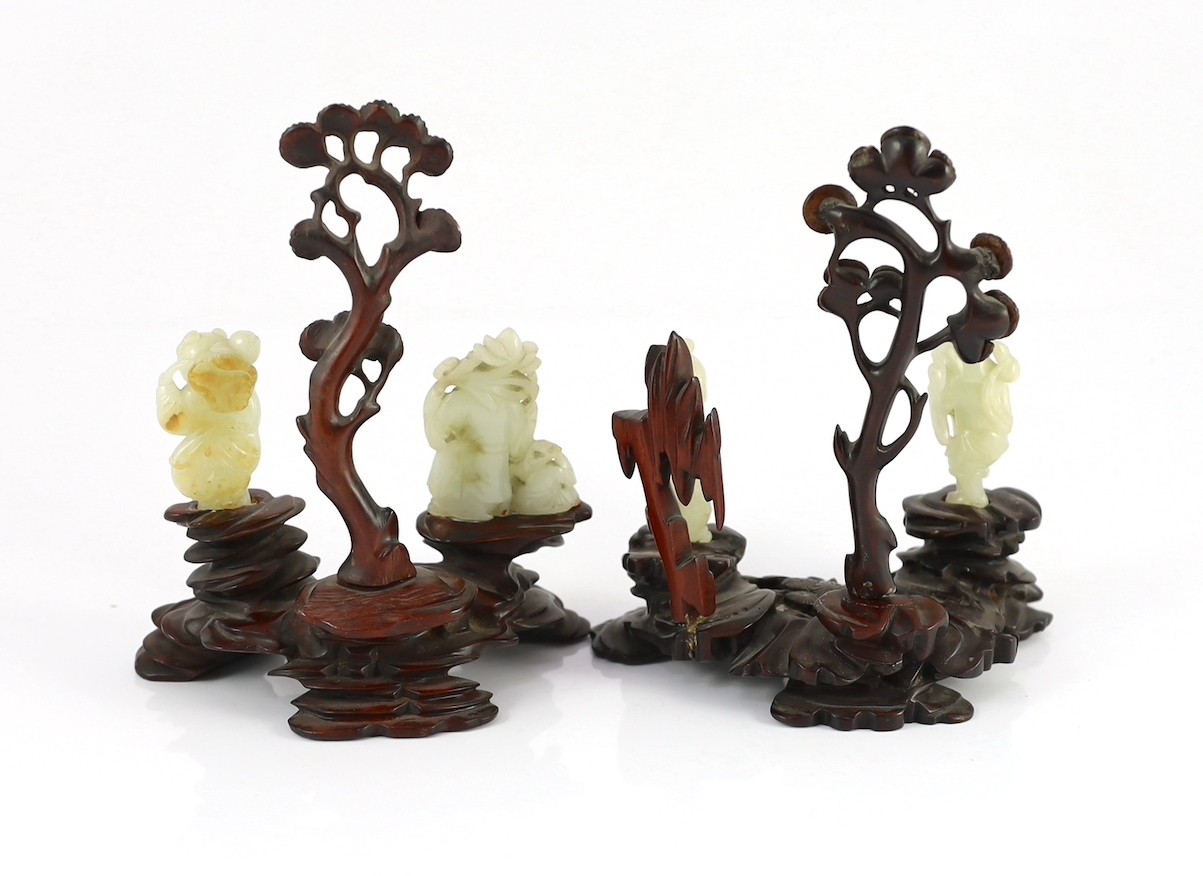 An assembled group of four Chinese pale celadon jade figures, 18th/19th century, displayed on two later wood 'rock-work' stands, total height approximately 19cm high